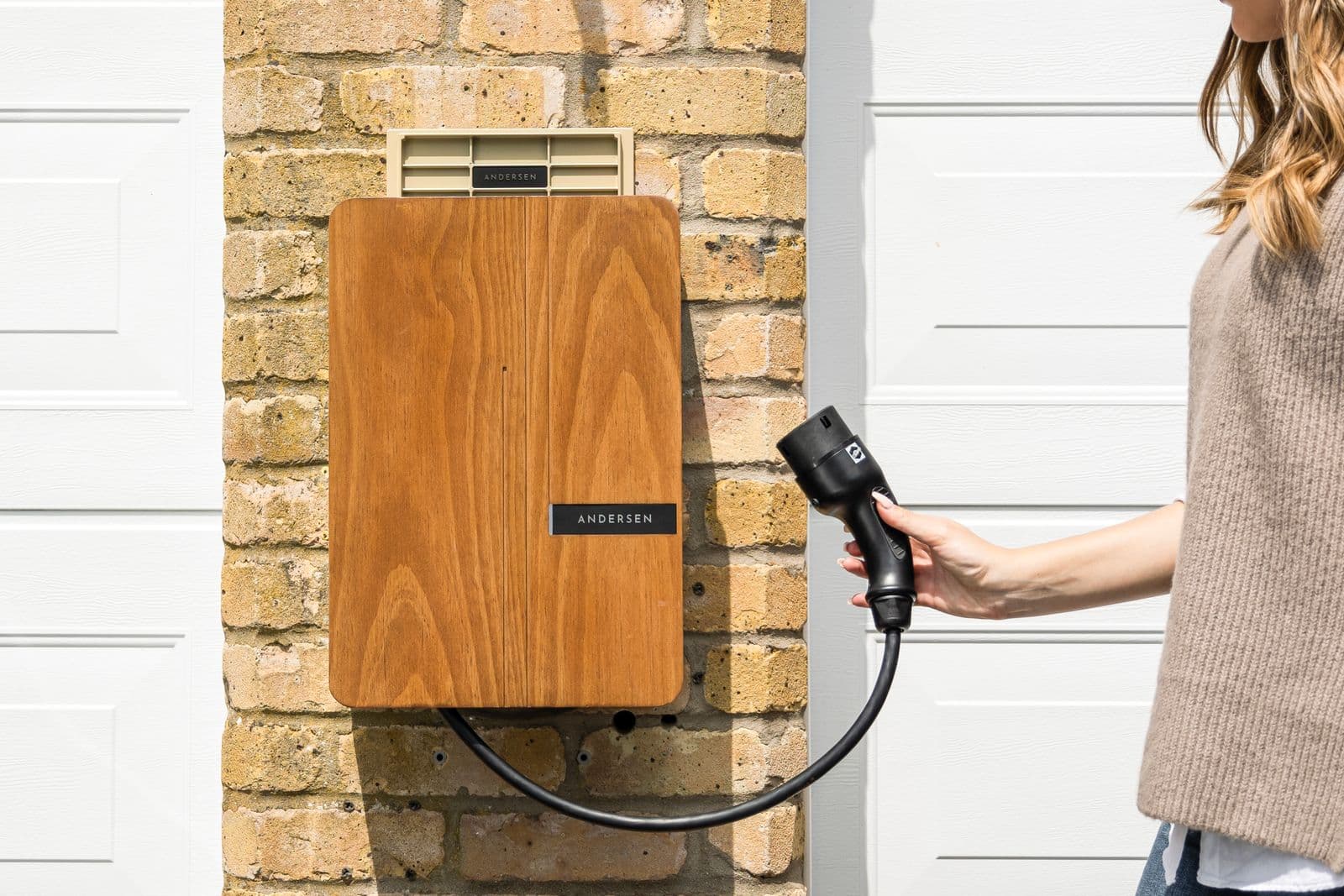 A wall-mounted home EV charger with the connector in hand
